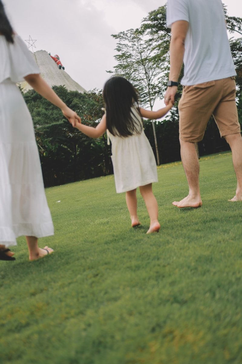 Family holding hands walking on grassy field.